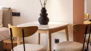 A modern room with a round table, two chairs, a vase with dried plants, a wall-mounted light, and a bed with a pillow. - Grid by Zoia Living (Athens)