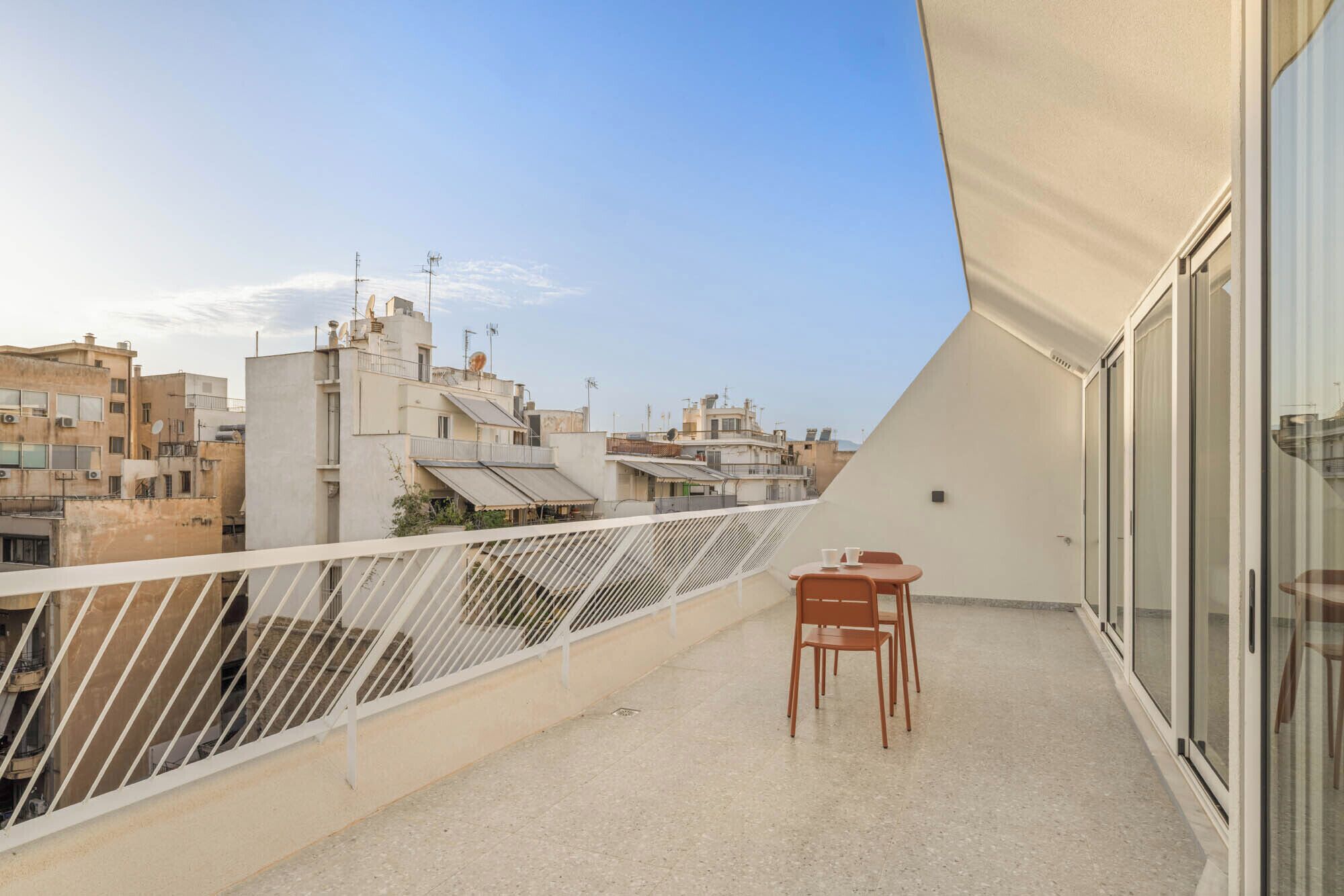 A balcony with a table and chairs, overlooking a cityscape with multiple buildings.
