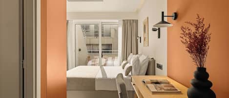 A modern hotel room with a bed, a dining table, and a vase of dried plants.