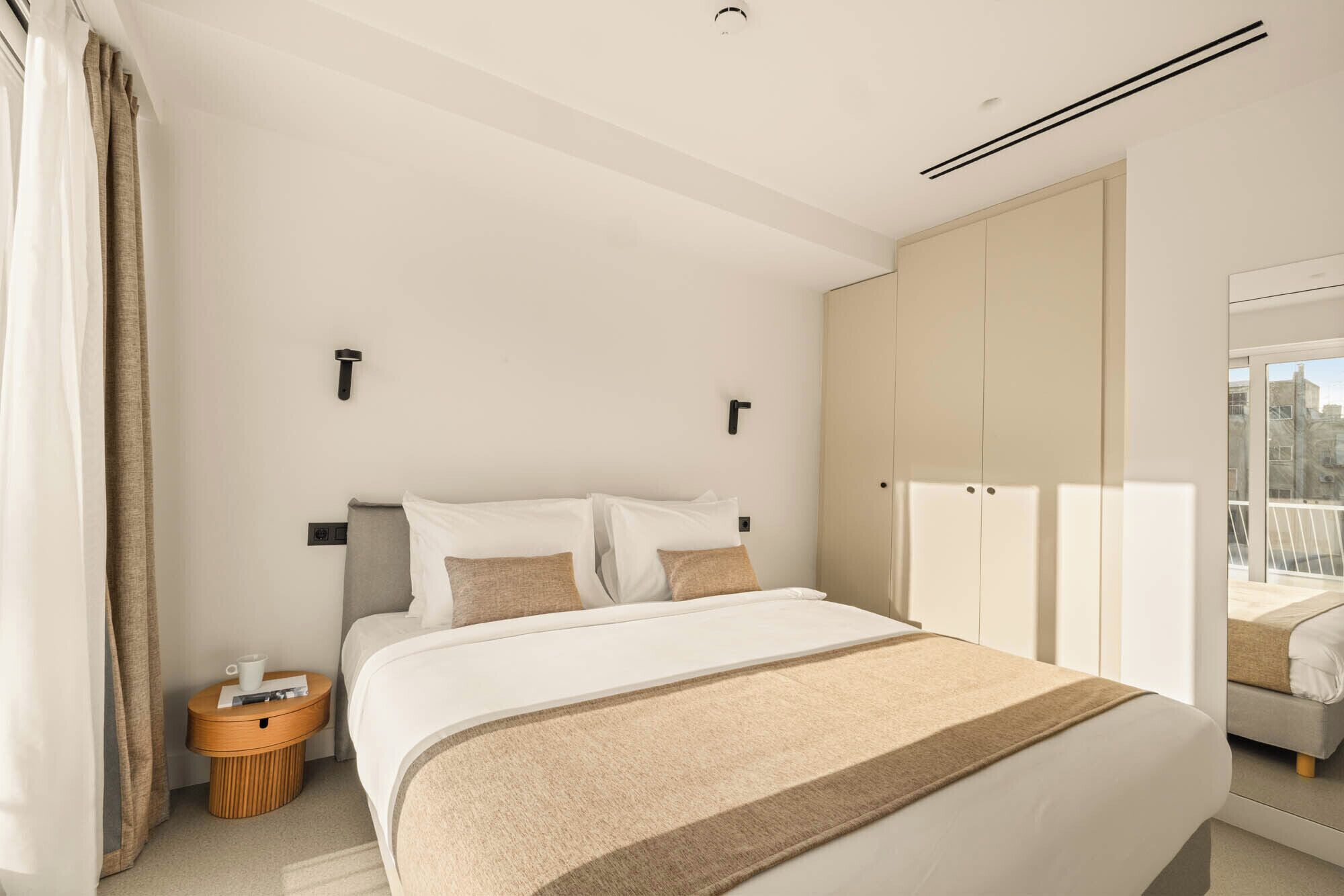 A modern hotel room with a large bed, a bedside table, and a wardrobe.