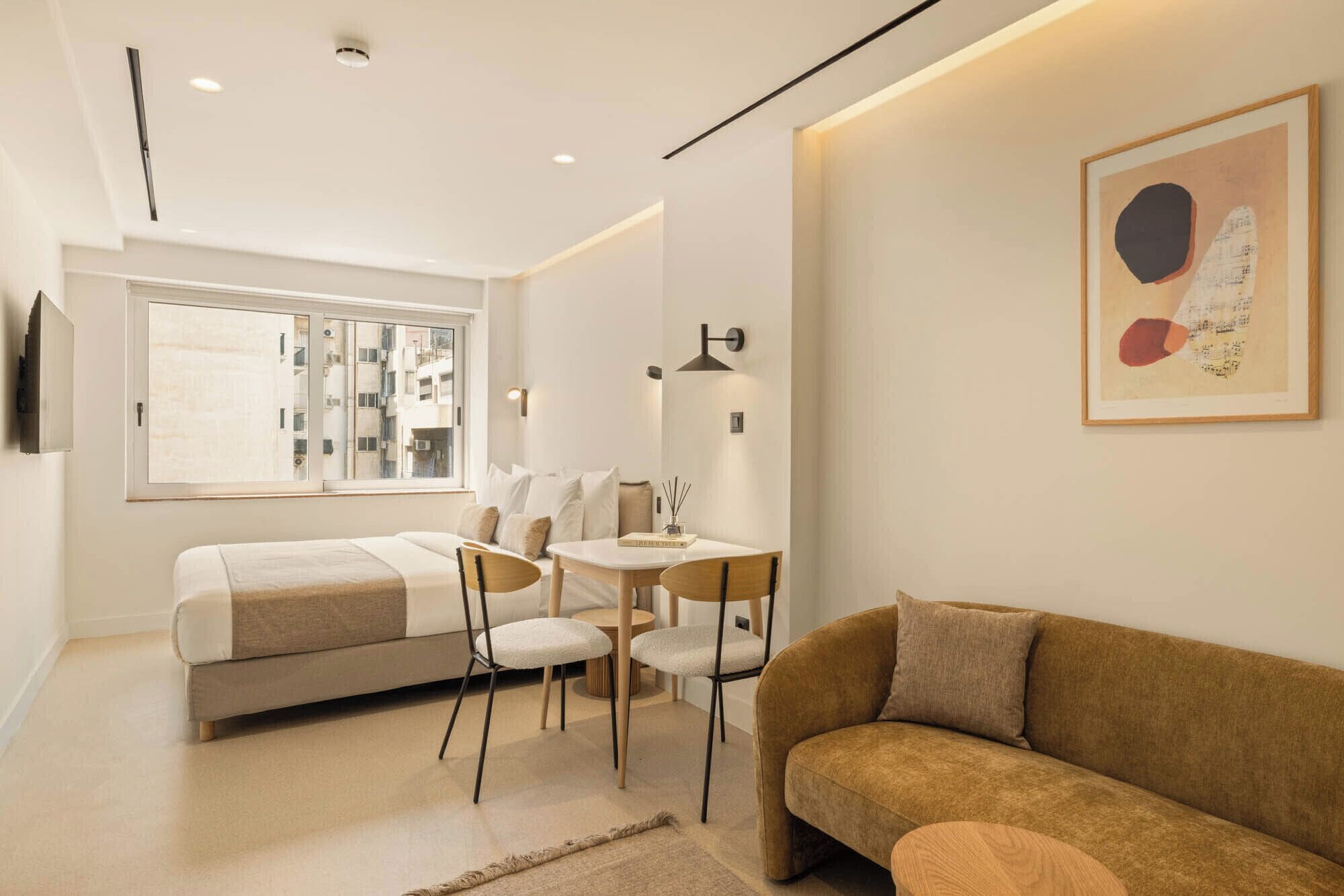 A modern hotel room with a bed, two chairs, a small table, and a sofa.