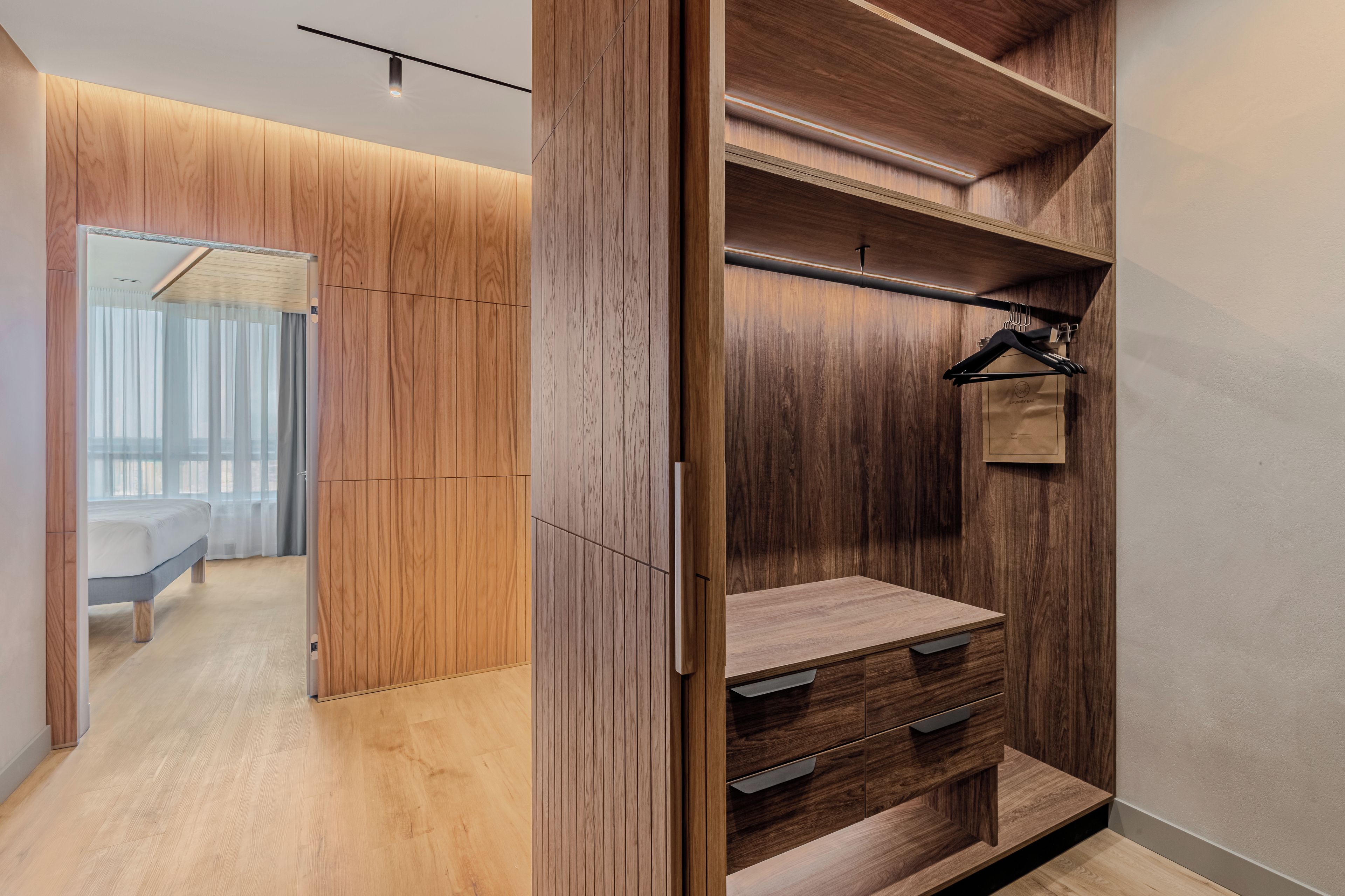 Un dressing moderne avec des panneaux en bois, une tringle à vêtements et un banc doté de tiroirs.