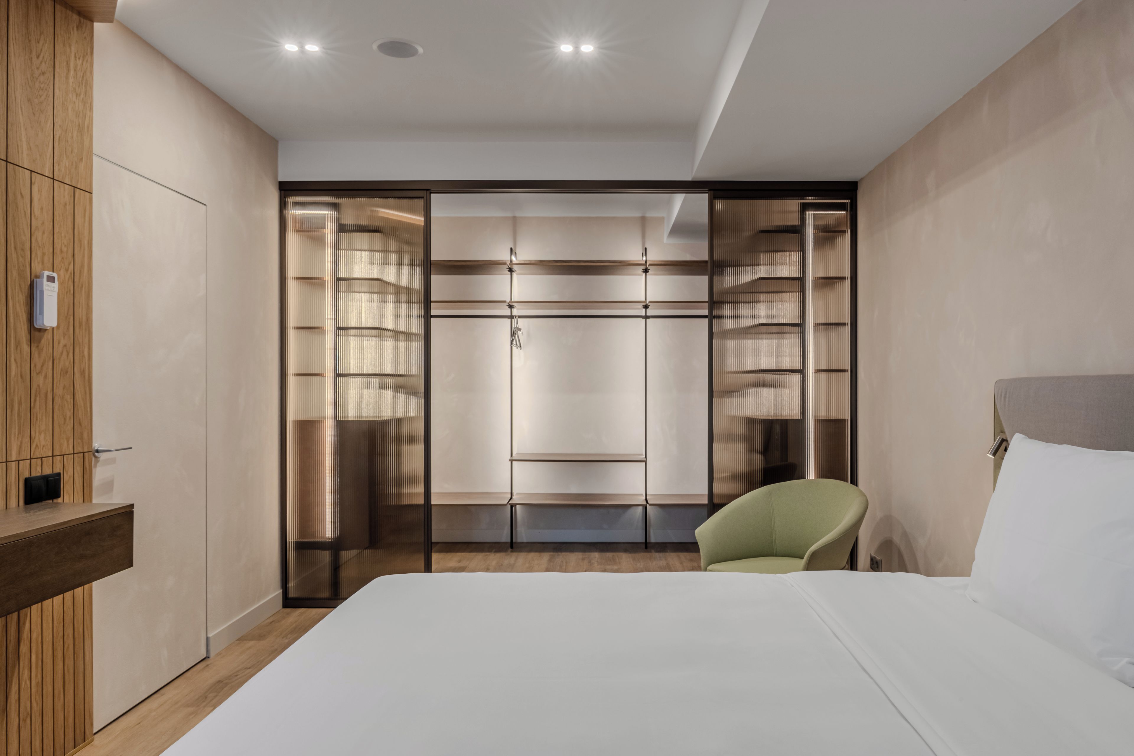 Een hotelkamer met een bed, een groene stoel, een kast en een spiegel.