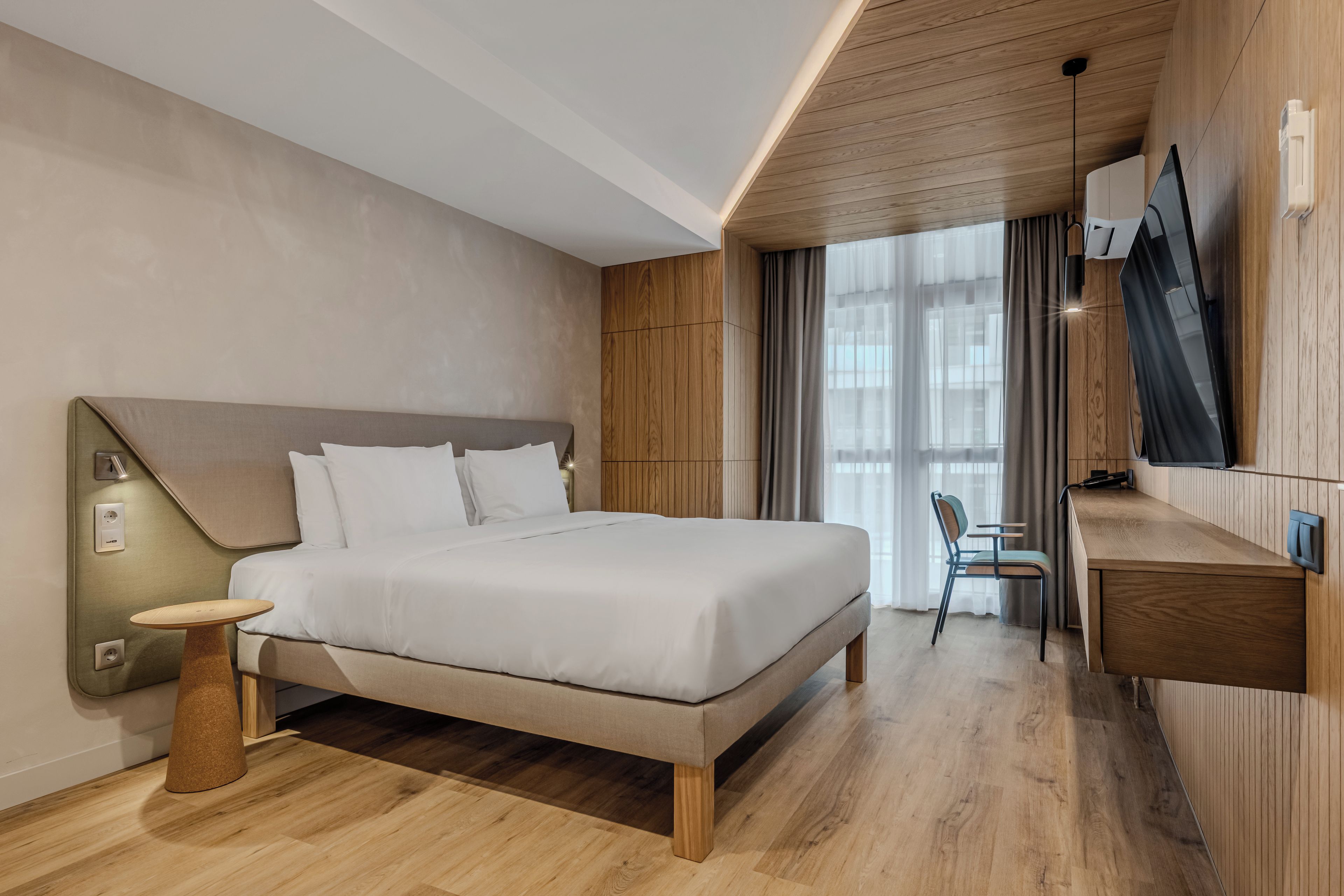 A modern hotel room with a large bed, a desk, and a television.