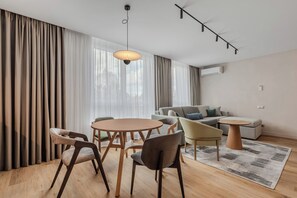 A modern living room with a dining area, featuring a sofa, chairs, a coffee table, and a hanging light fixture.