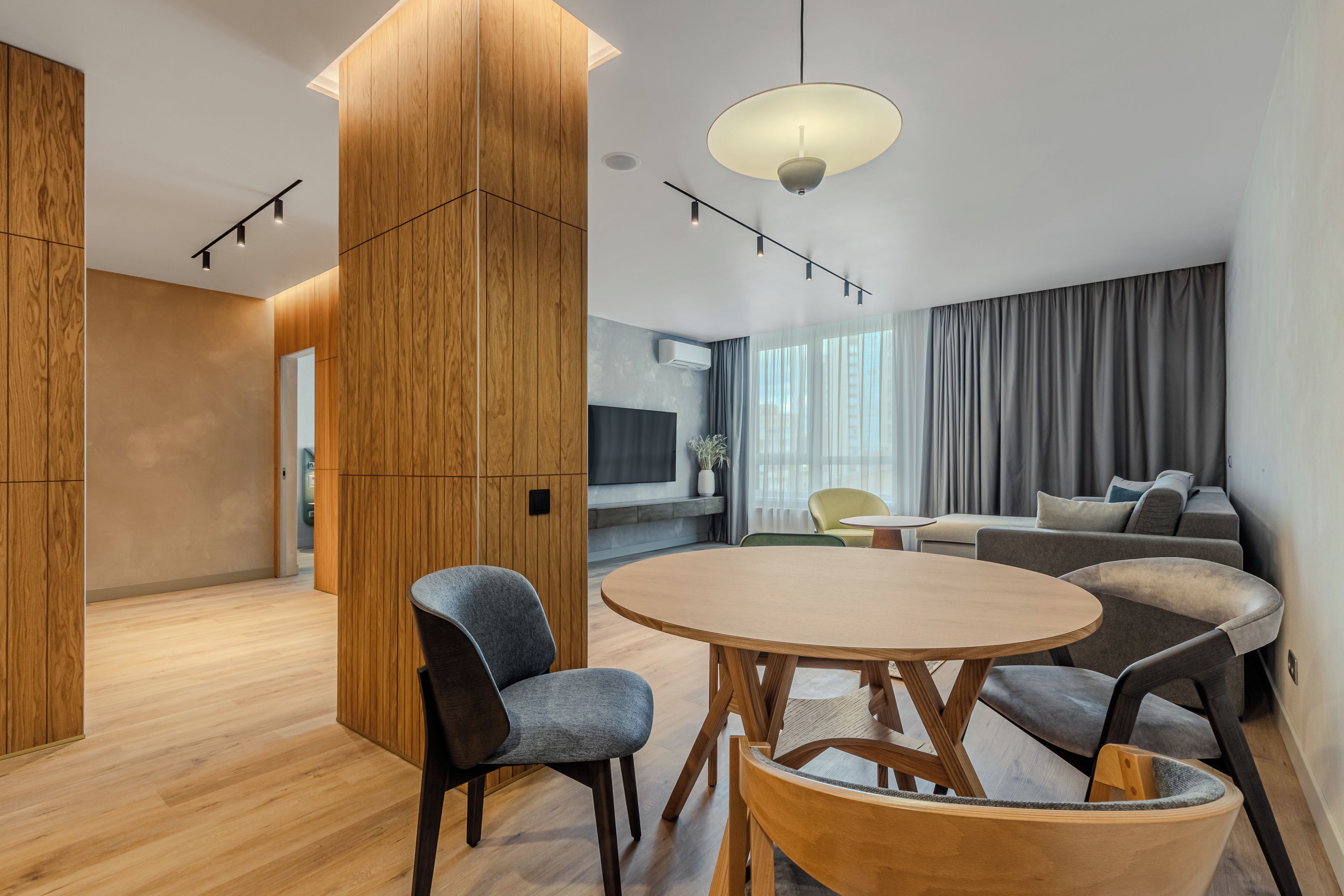 Un salon moderne avec une table ronde en bois, deux chaises, un canapé et une grande fenêtre avec des rideaux.