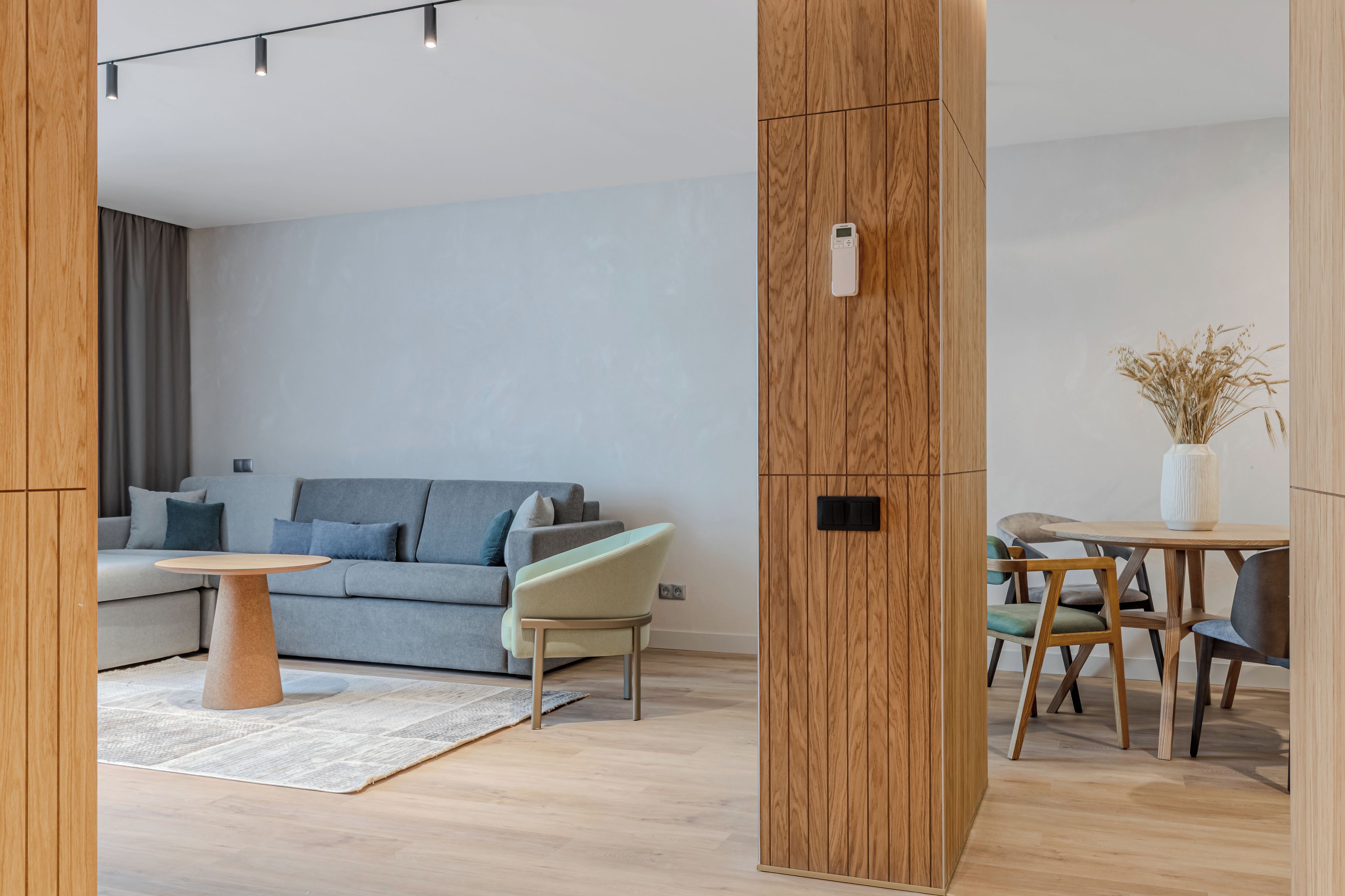 Een moderne woonkamer met een grijze bank, een klein rond tafeltje en een eethoek met een houten tafel en stoelen.