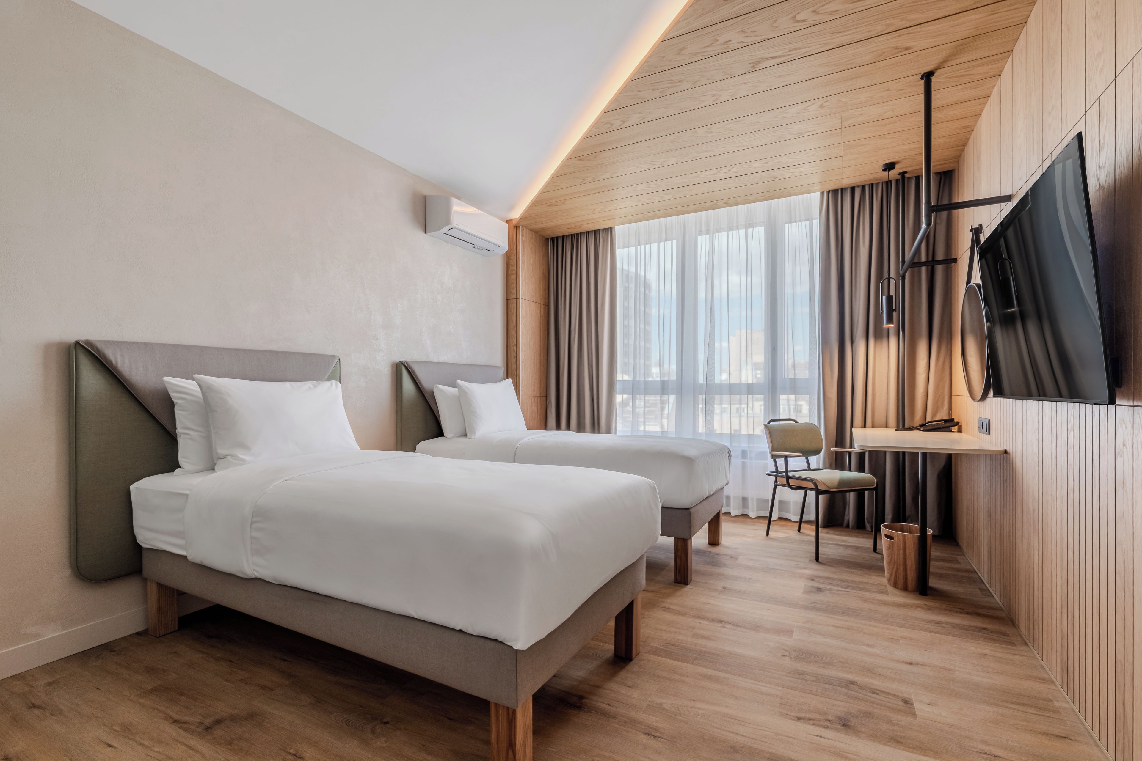 Habitación de hotel con dos camas, un escritorio, una silla, un televisor y un ventanal con cortinas.