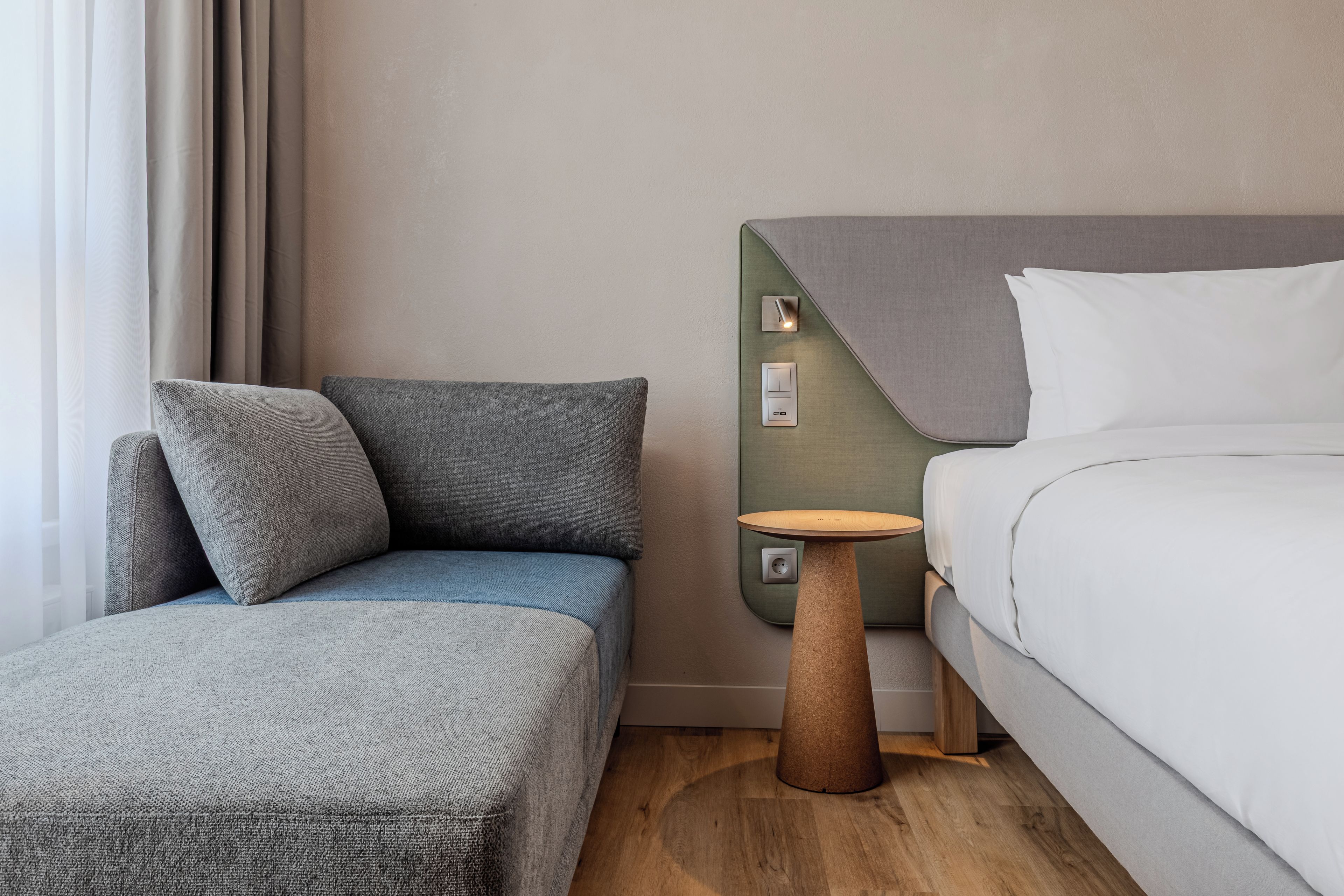 A modern hotel room with a bed, a small table, and a seating area with cushions.
