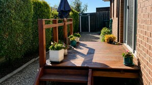 Eine Holzdielen-Terrasse mit Kübelpflanzen, ein Holzzaun und eine Backsteinmauer.