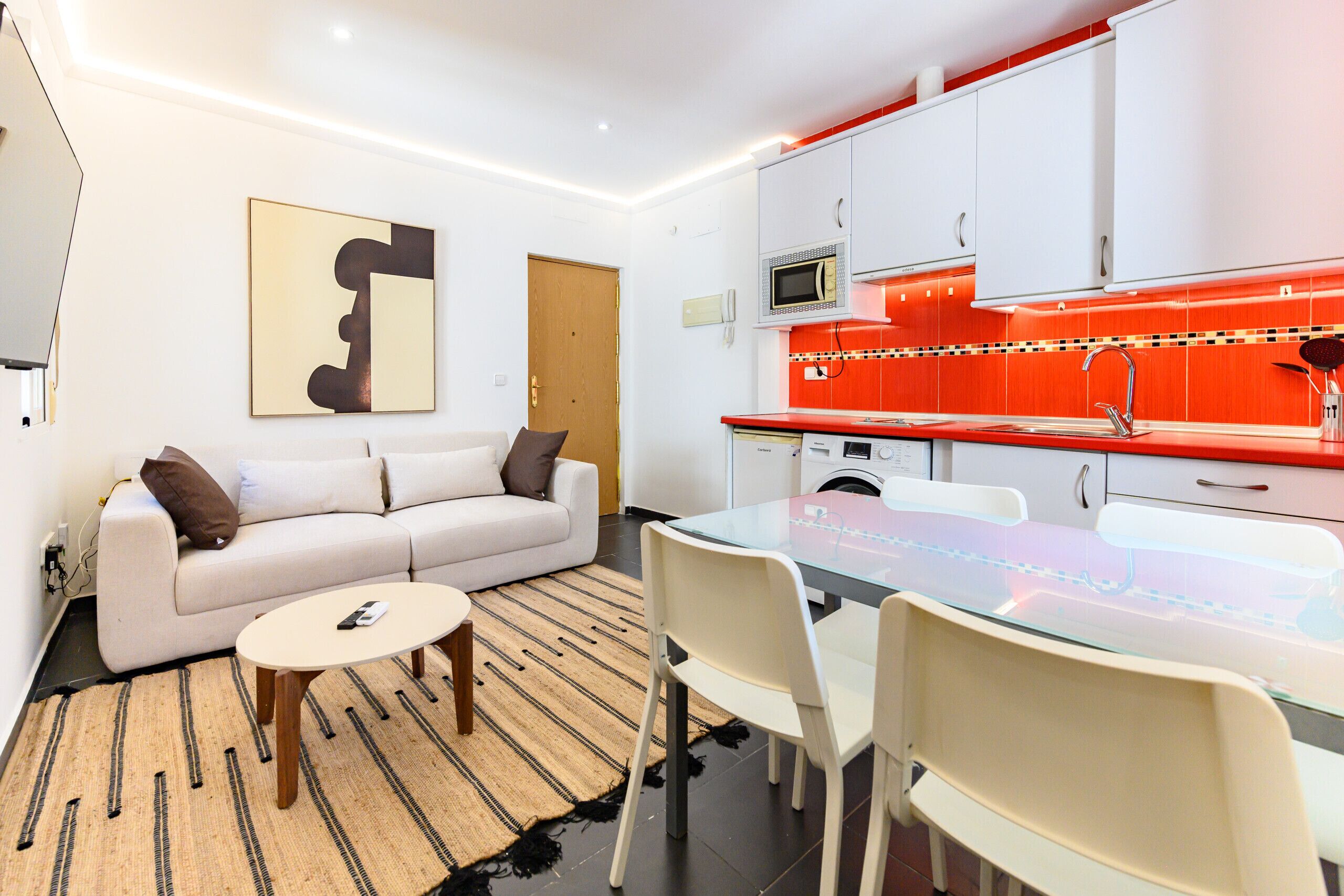 A modern kitchen with white cabinets, a microwave, and a red backsplash.