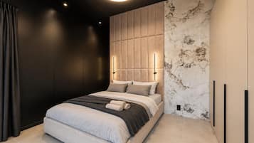 A modern bedroom with a bed, a headboard with built-in lighting, and a marble-patterned wall.