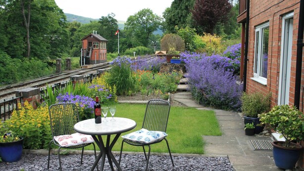 A garden with a table and chairs, a small building, and a pathway. - Railway & Riverside Retreat (Llangollen)