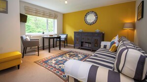 A living room with a sofa, a dining table, chairs, a fireplace, and a view through a window. - Railway & Riverside Retreat (Llangollen)