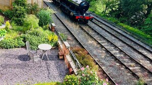A steam locomotive on a railway track surrounded by lush greenery and a small garden area with a table and chairs. - Railway & Riverside Retreat (Llangollen)