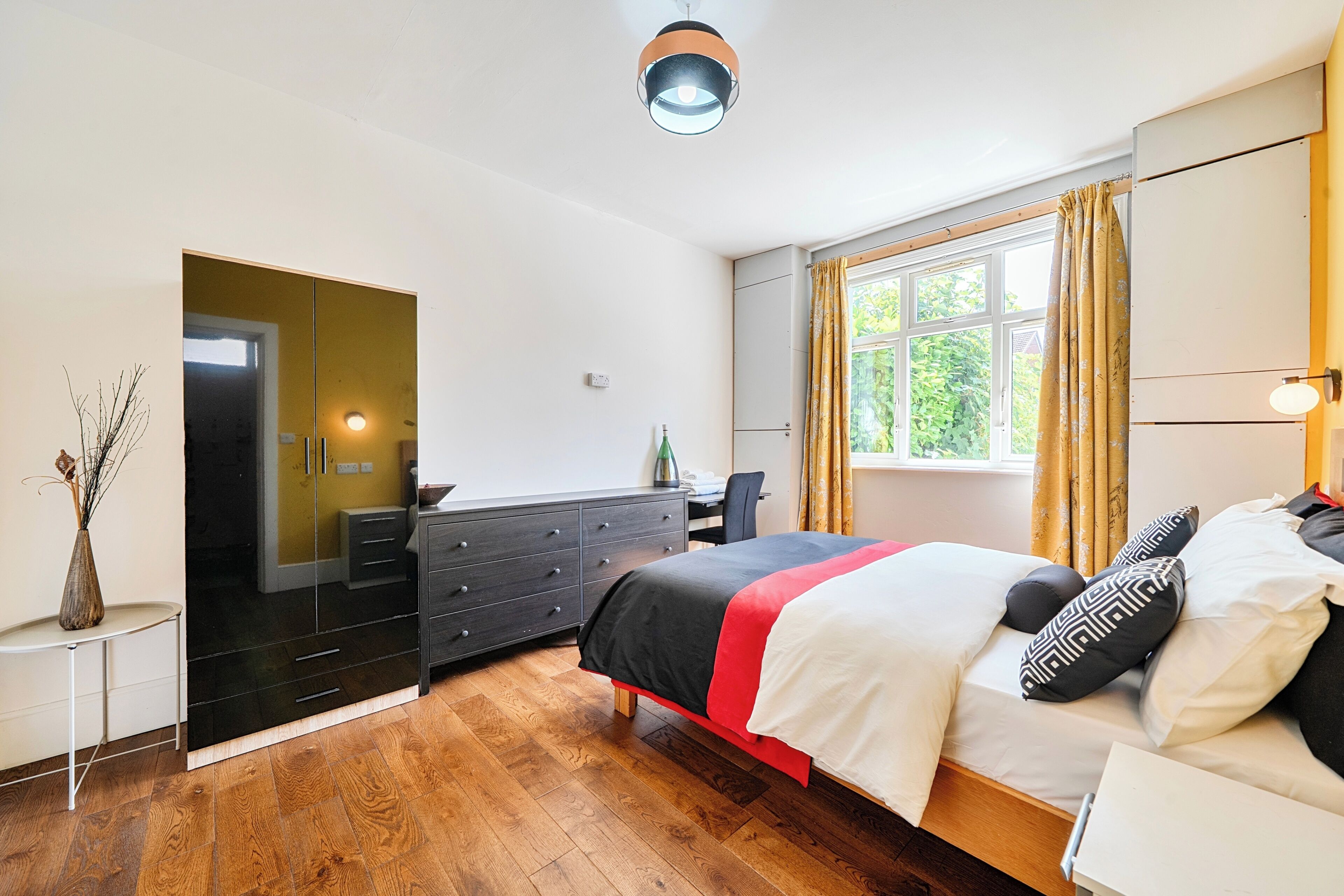 A bedroom with a bed, a desk, a wardrobe, and a window with curtains.
