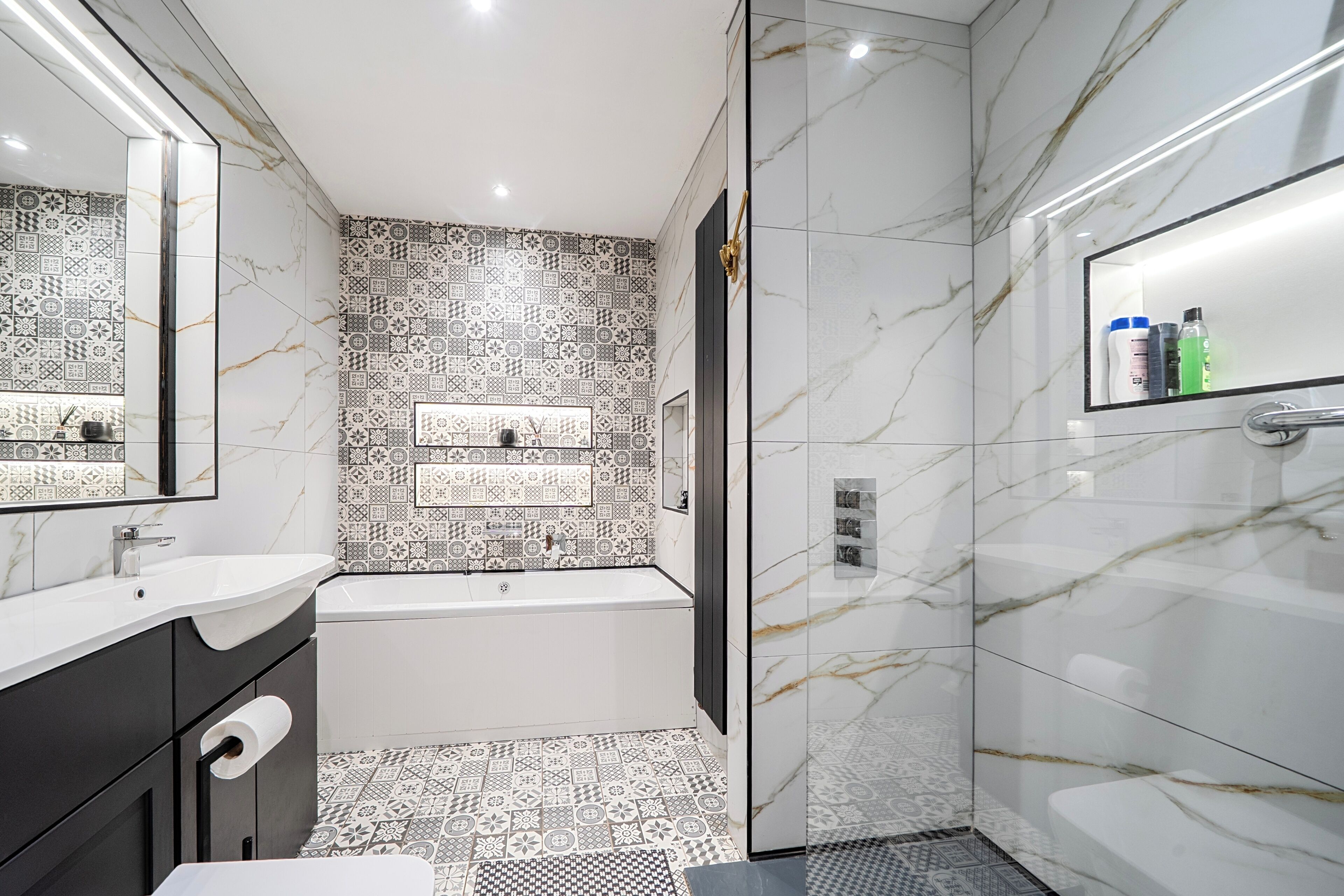 A modern bathroom with a bathtub, a large mirror, and patterned tiles.