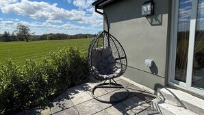 Eine Terrasse mit einer Hängematte, Steinplattenboden und einem Gebäude mit Fenster und Wandleuchte.