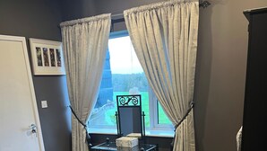 Ein Schlafzimmer mit Bett, Schreibtisch mit Stuhl, einem Fenster mit Vorhängen und einem Spiegel.