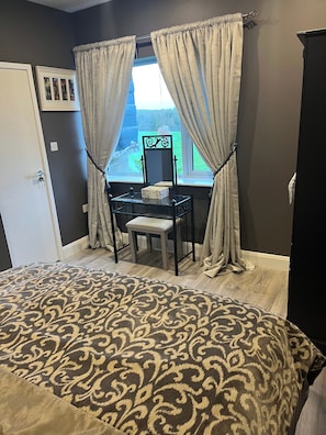A bedroom with a bed, a desk with a chair, a window with curtains, and a mirror.