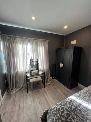 Une chambre à coucher comprenant un lit, un bureau avec une chaise, une armoire et une fenêtre avec des rideaux.