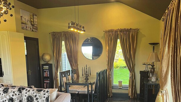 Ein Wohnzimmer mit einer Couch, einem Esstisch, einer Deckenleuchte und Blick ins Freie.