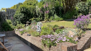 A garden with a brick wall, a statue, and a variety of plants. - Bungalow - Sleeps 2 - Parking (Newquay)
