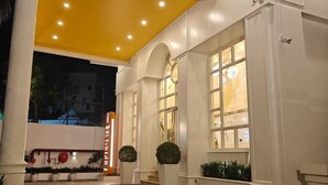 Entrada de un hotel con un toldo amarillo, columnas blancas y un camino pavimentado.