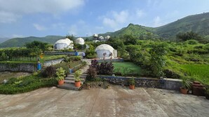 Un resort con varias construcciones abovedadas, un área pavimentada con plantas en macetas y montañas al fondo.
