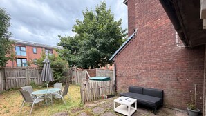 A backyard with a brick wall, a wooden fence, a table with chairs, a sofa, and a small garden area.