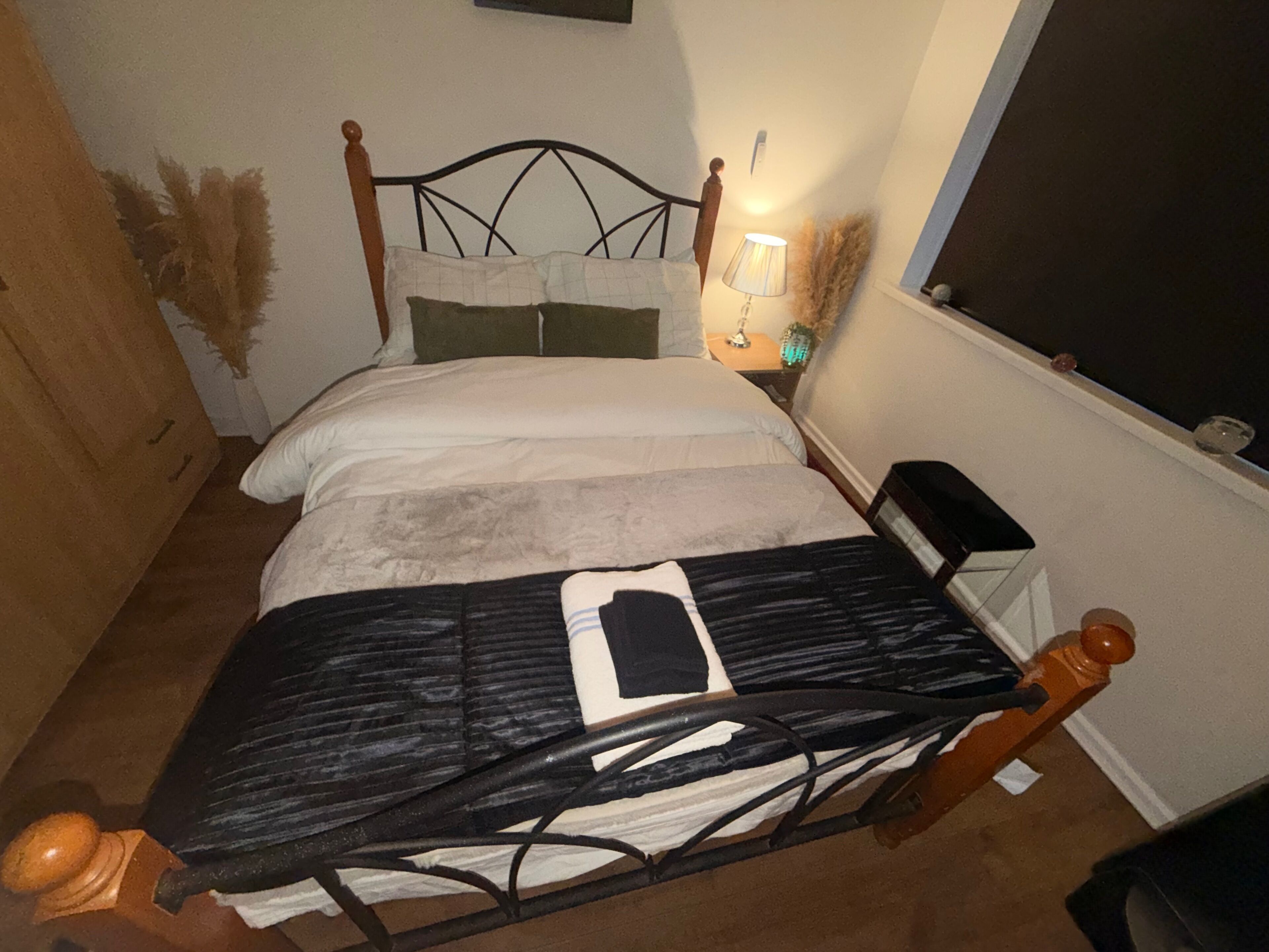 A single bed with a metal frame, a bedside table with a lamp, and a window with a view of the outside.