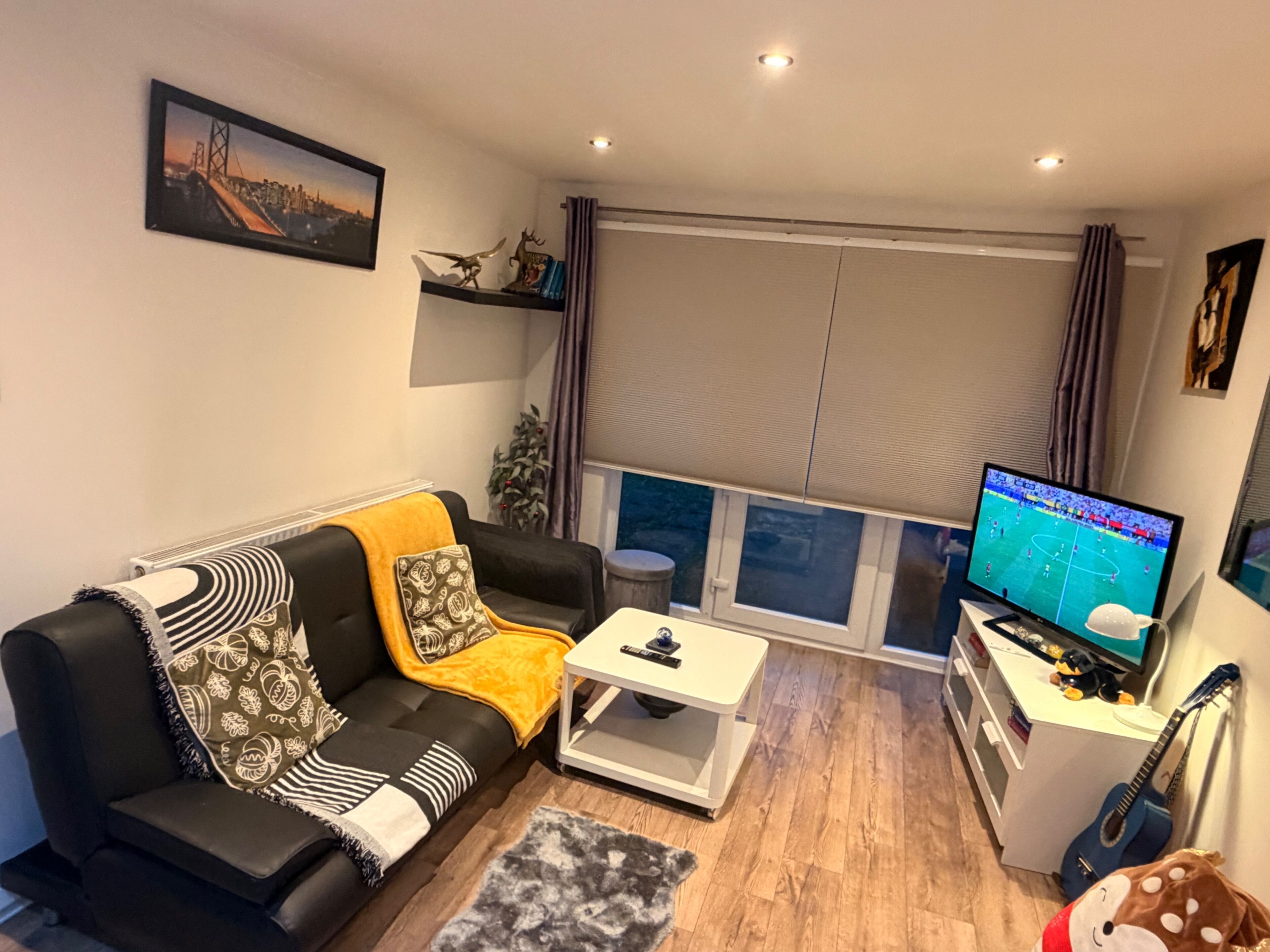 A living room with a sofa, coffee table, TV, and a guitar.