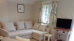 A living room with a sectional sofa, a small side table, a flat-screen TV, and a patterned rug. - The Barn, Enstone - a Cosy Cotswolds Retreat (Chipping Norton)