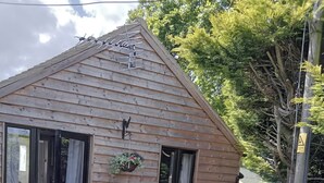 A wooden cabin with a sliding glass door, a small window, and a patio with a table and chairs. - The Barn, Enstone - a Cosy Cotswolds Retreat (Chipping Norton)