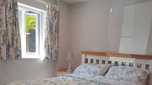 A bedroom with a bed, a window with curtains, a bedside lamp, and a view of greenery outside. - The Barn, Enstone - a Cosy Cotswolds Retreat (Chipping Norton)