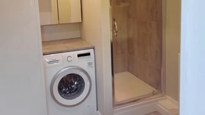 A compact laundry room with a washing machine, a shower, and a mirror. - The Barn, Enstone - a Cosy Cotswolds Retreat (Chipping Norton)