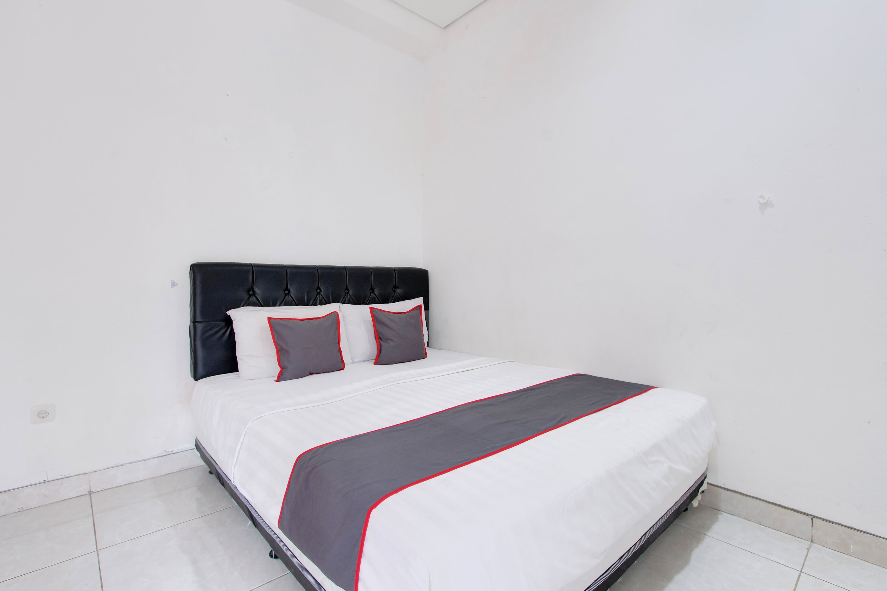 Un lit bien fait, avec une couvre-lit grise et rouge, une tête de lit noire et deux oreillers.