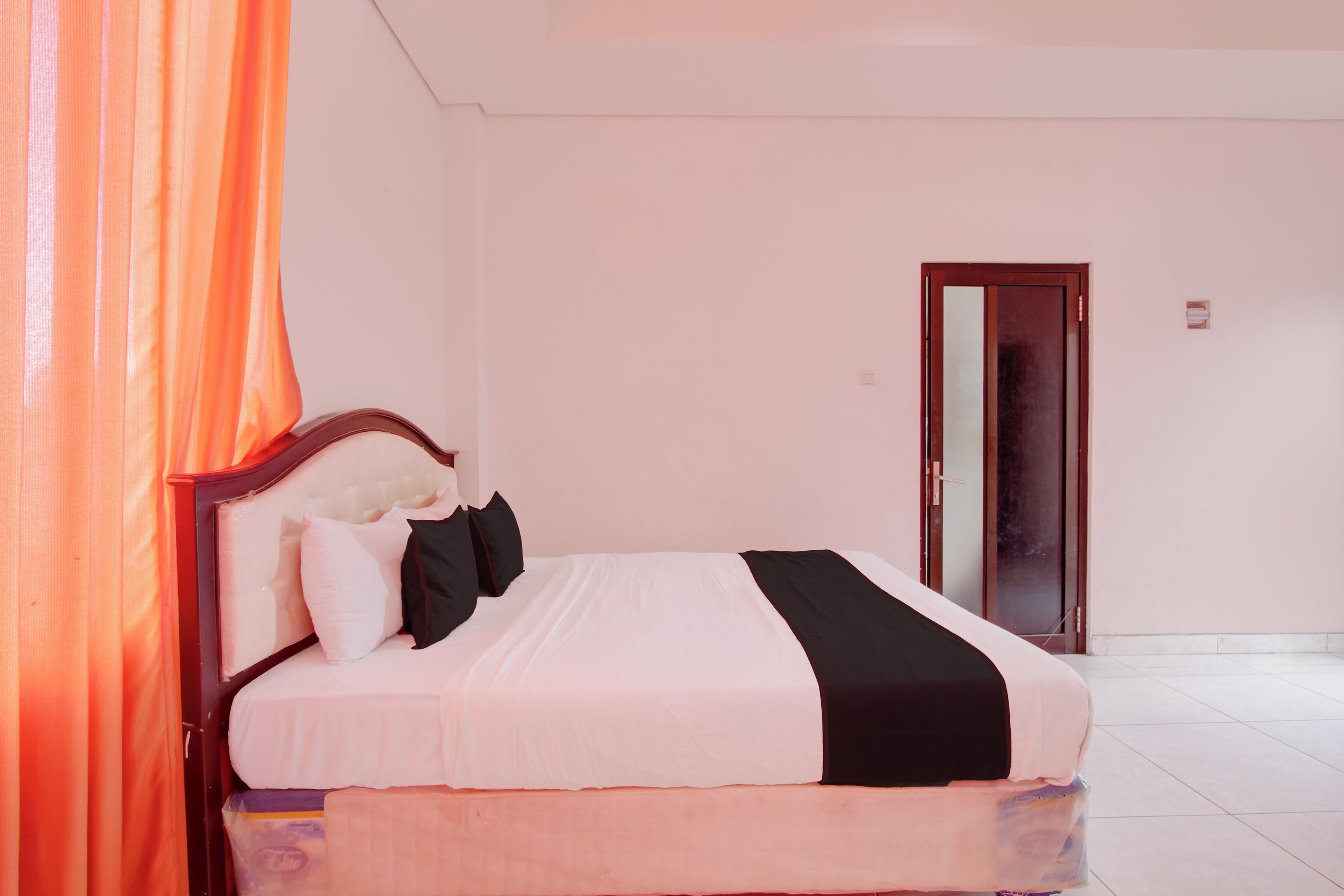 A hotel room with a bed, curtains, a door, and a tiled floor.