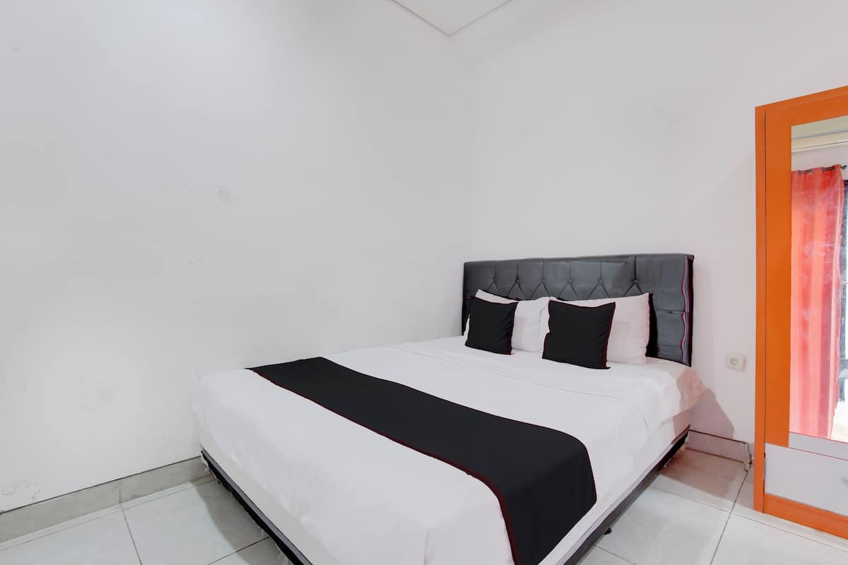 A neatly made bed with a black and white bedspread and a red accent, a grey upholstered headboard, and a white wall with a small window.