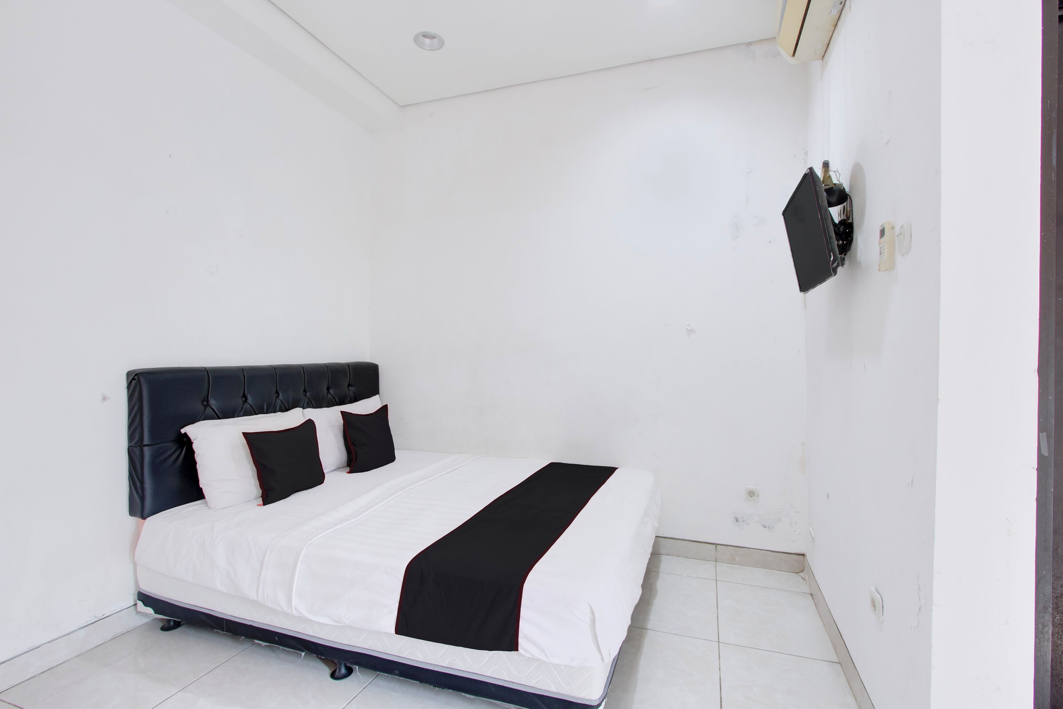 A bedroom with a bed, a wall-mounted TV, and a door.