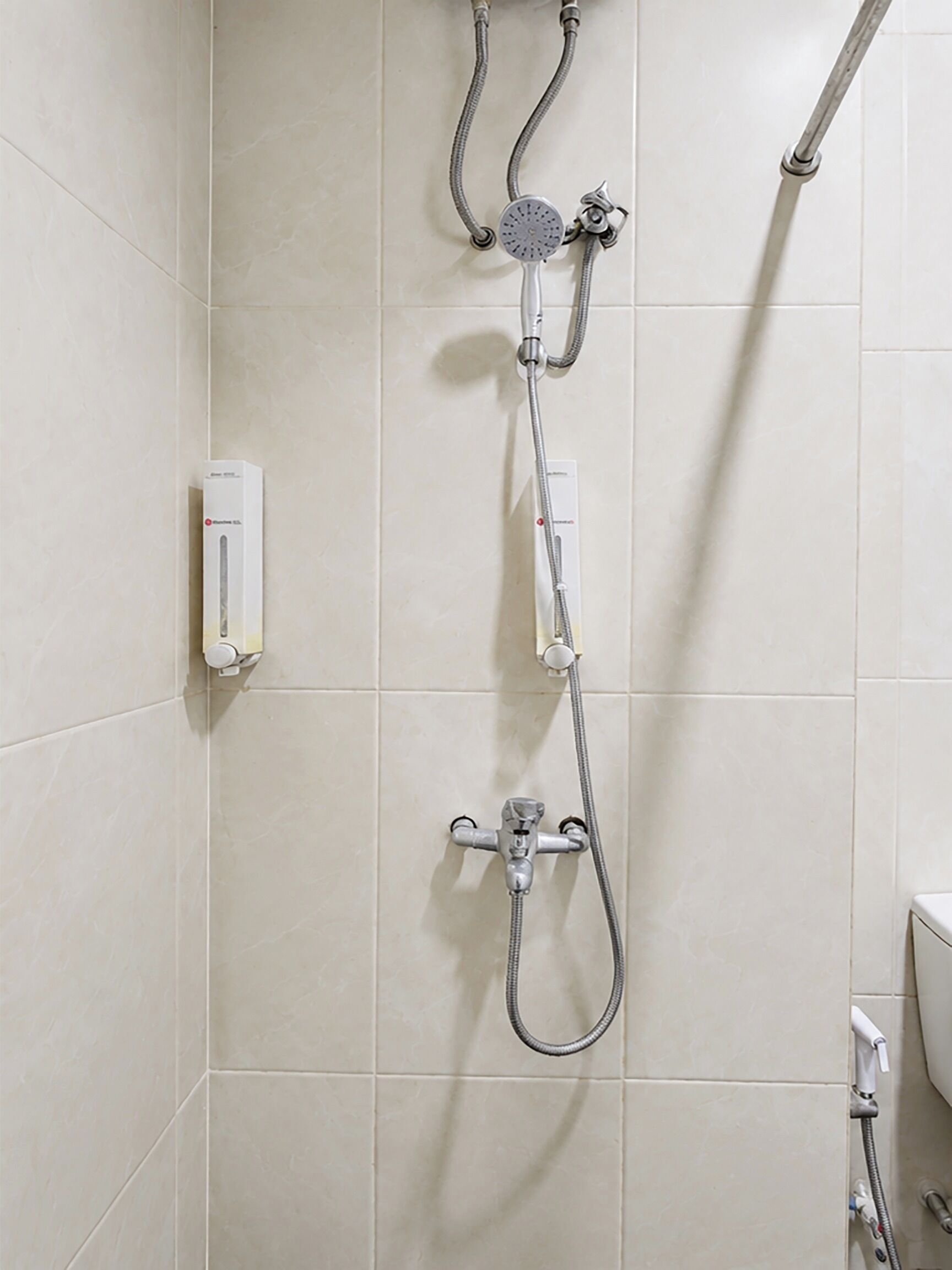A shower with a handheld showerhead and a wall-mounted faucet, both with hoses.