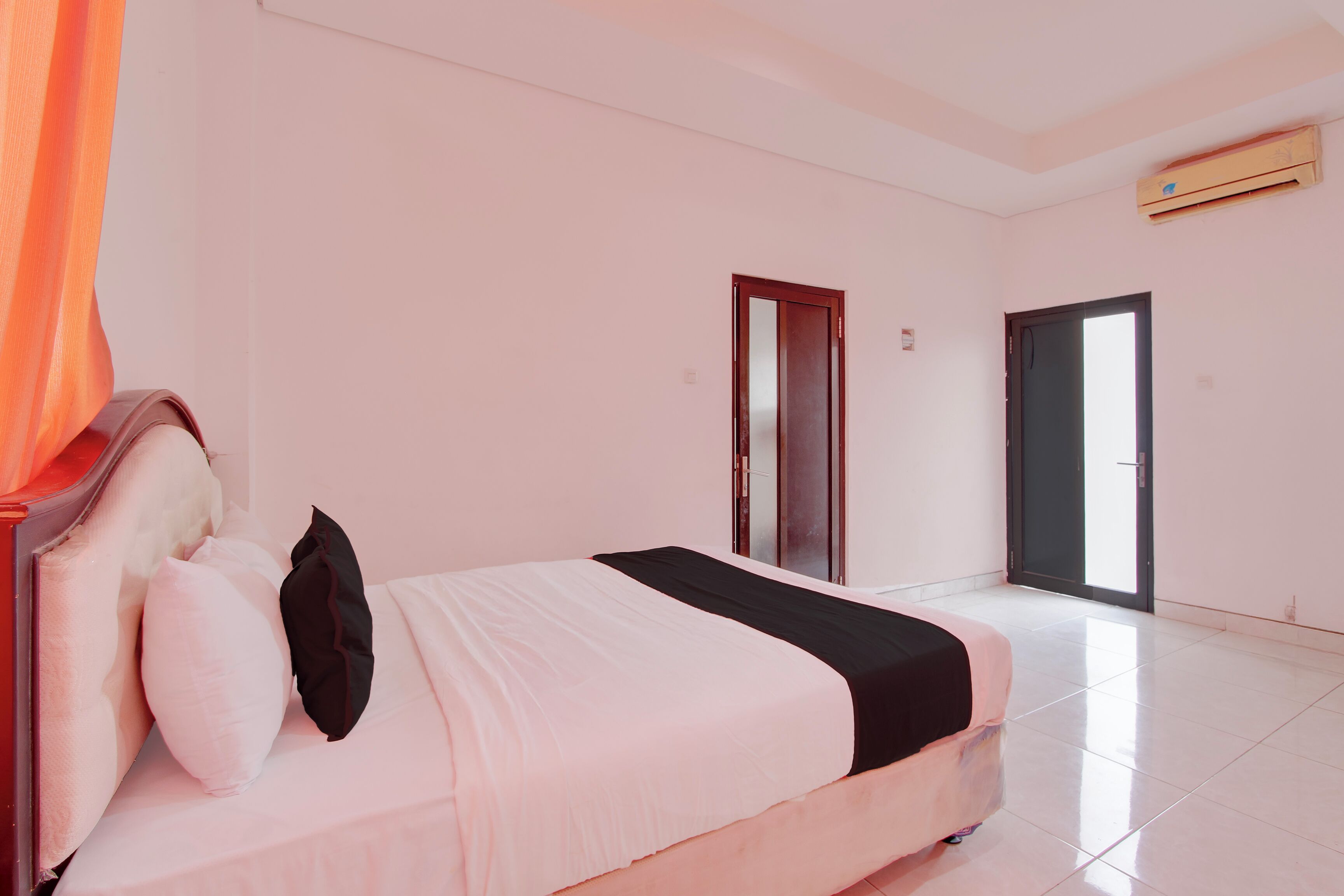 A bedroom with a bed, pillows, a door, and an air conditioning unit.
