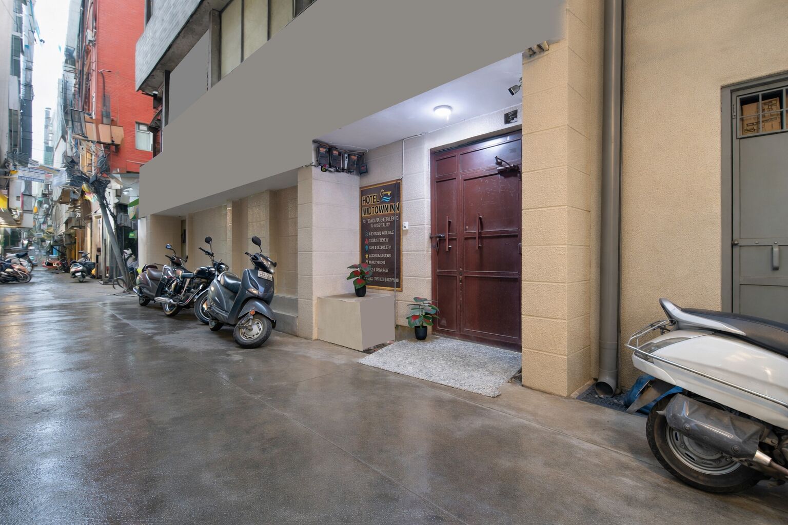 L’entrée d’un hôtel, avec une porte fermée, une enseigne et plusieurs scooters garés.