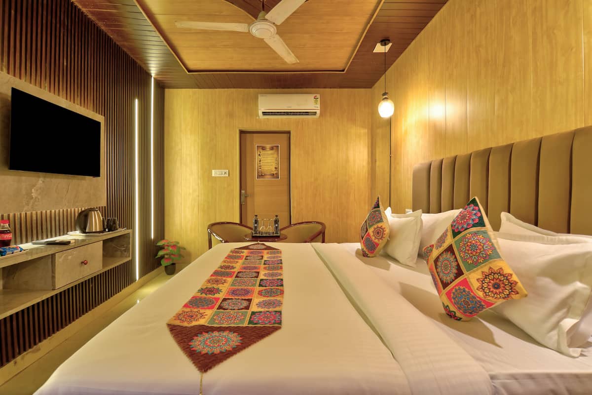 A hotel room with a bed, a TV, a desk with a kettle, and a ceiling fan.