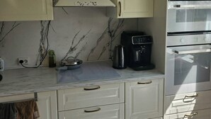 Una cocina con armarios blancos, salpicadero de mármol, campana extractora, cafetera y horno.