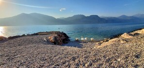 Ein Kiesstrand mit einem Felsen und weiter Aussicht auf entfernte Berge.