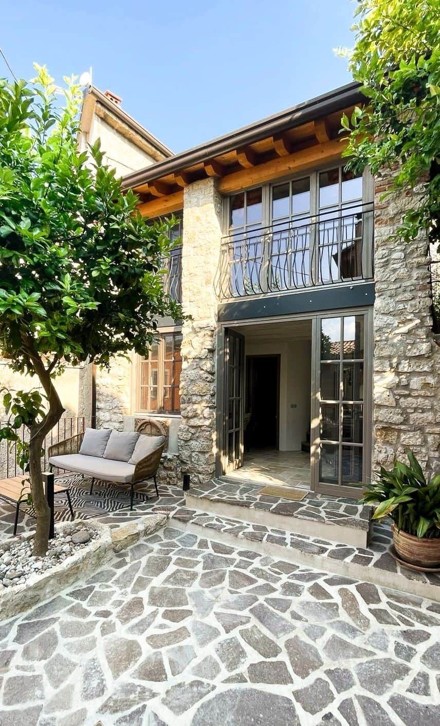 Une terrasse en pierre avec un espace salon intégré et un arbre.