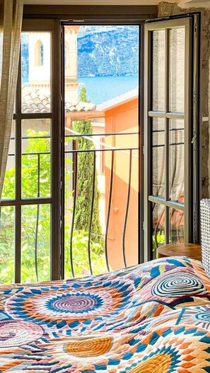 Ein Zimmer mit einem Bett, einem Fenster mit Blick auf ein Gebäude und Wasser, sowie einem Balkon mit Geländer.