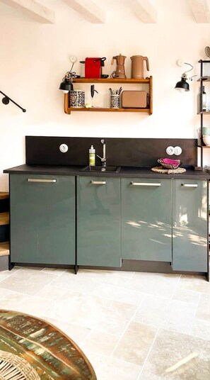 A kitchen with a dark cabinet, a shelf with kitchen items, and a hanging lamp. - Casa Limone – just steps from the lake (Castelletto)