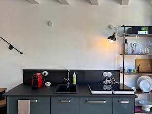 A modern kitchen with a black countertop, a sink, a red kettle, a coffee maker, a stove, and a shelf with kitchenware. - Casa Limone – just steps from the lake (Castelletto)